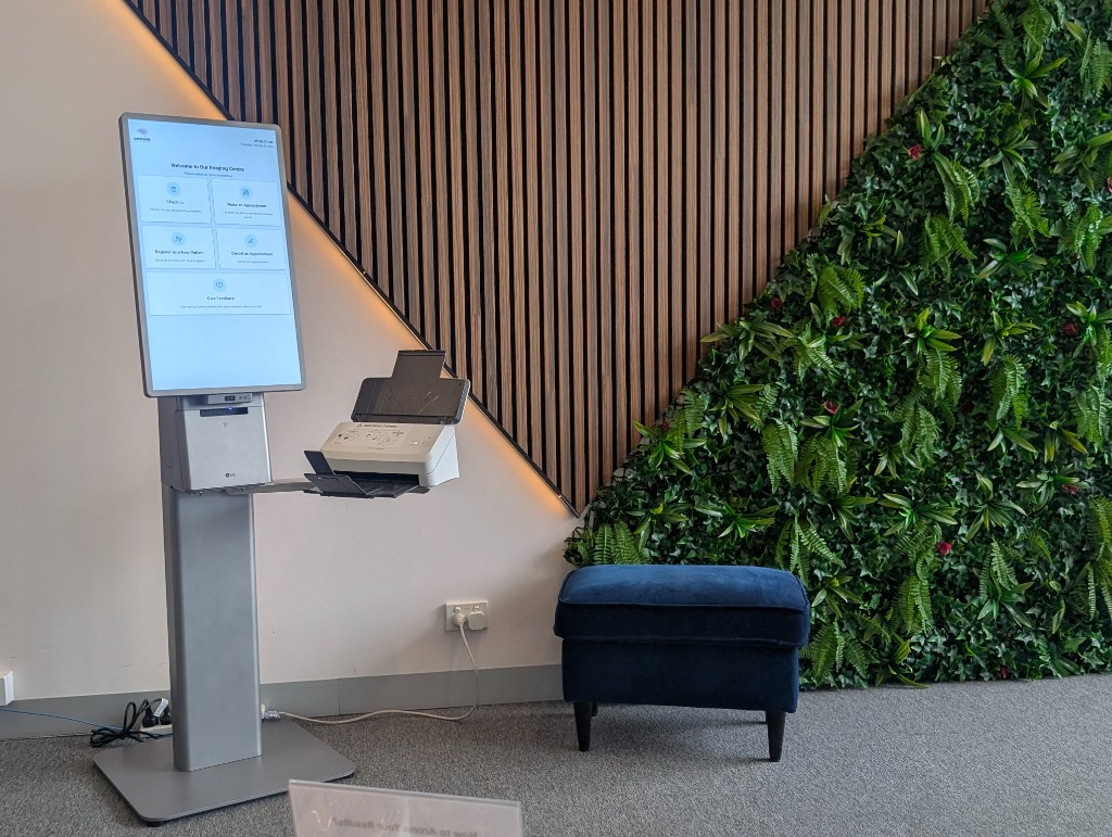 Kiosco de autoservicio en clínica de imagen: pantalla vertical con menú de bienvenida y escáner de documentos